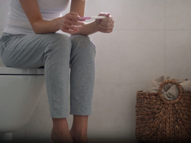 woman with pregnancy test sitting in bathroom