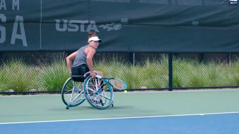 A Woman in A Tennis Wheelchair, Dressed in Sports Attire, Poised and Focused as She Prepares to Hit a Tennis Ball on The Court