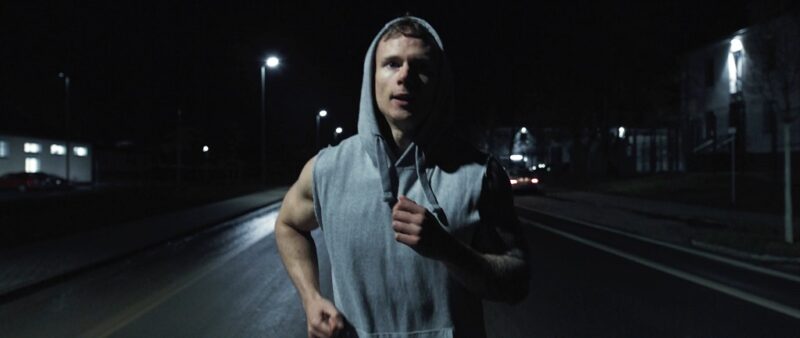Young athletic man jogging at night on a dimly lit road, wearing a hoodie