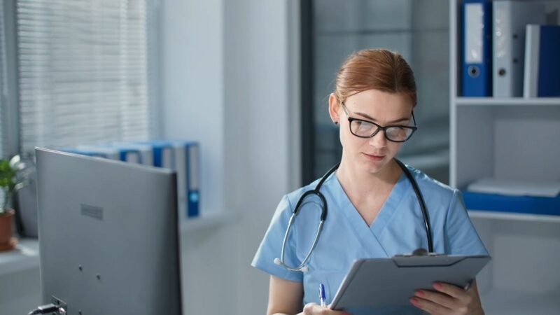 Female doctor or nurse reviewing patient documents on a clipboard in a hospital office