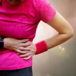 A woman in workout clothes holds her side during exercise, showing signs of lower rib pain