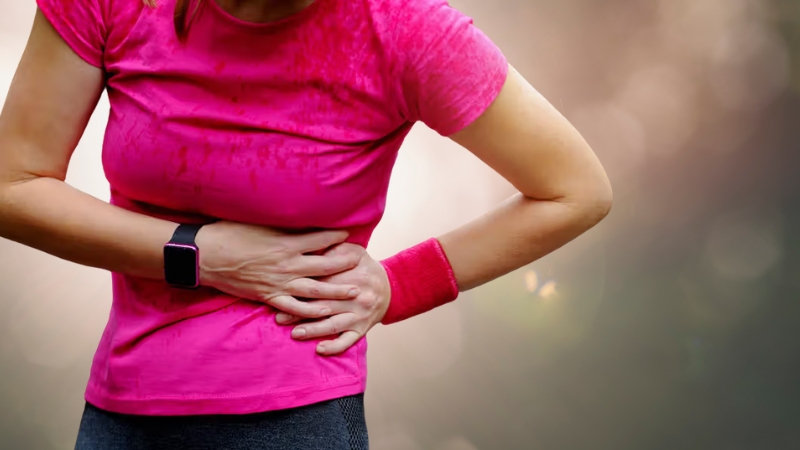 A woman in workout clothes holds her side during exercise, showing signs of lower rib pain