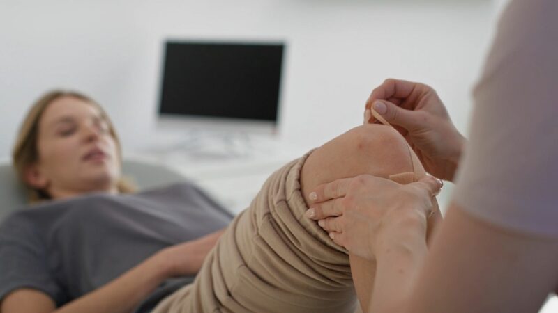 Physician applying medical tape on a patient’s knee during arthritis treatment