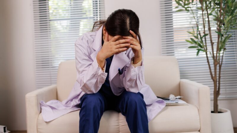 A tired doctor sits with her head in her hands after a difficult day at the clinic