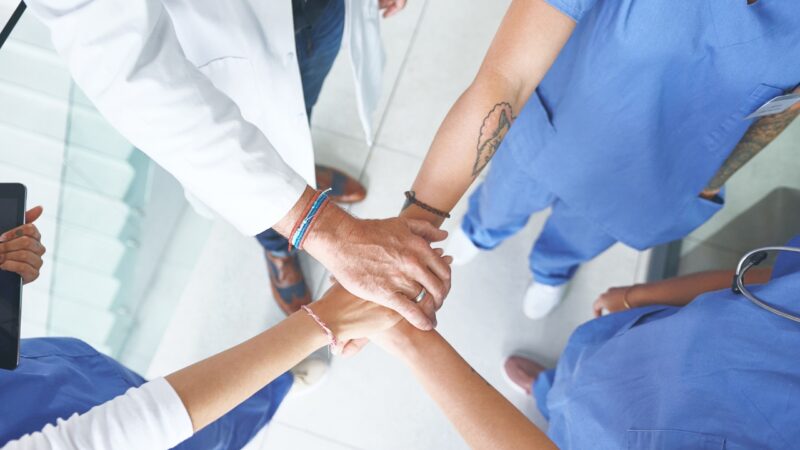 A medical team joins hands to show coordinated care in a clinic
