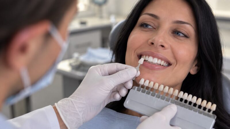 Dentist comparing a shade guide with a patient’s front teeth.